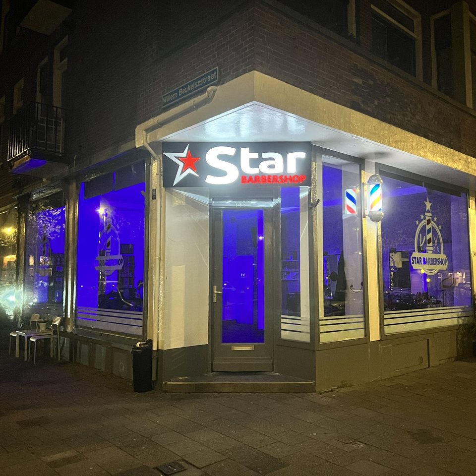 Star Barbershop's corner storefront lit up at night, with its neon sign and blue-lit windows