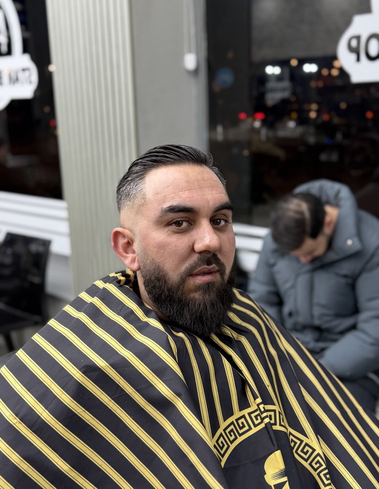 Client with a slicked-back cut and a full, shaped beard in the barber's chair