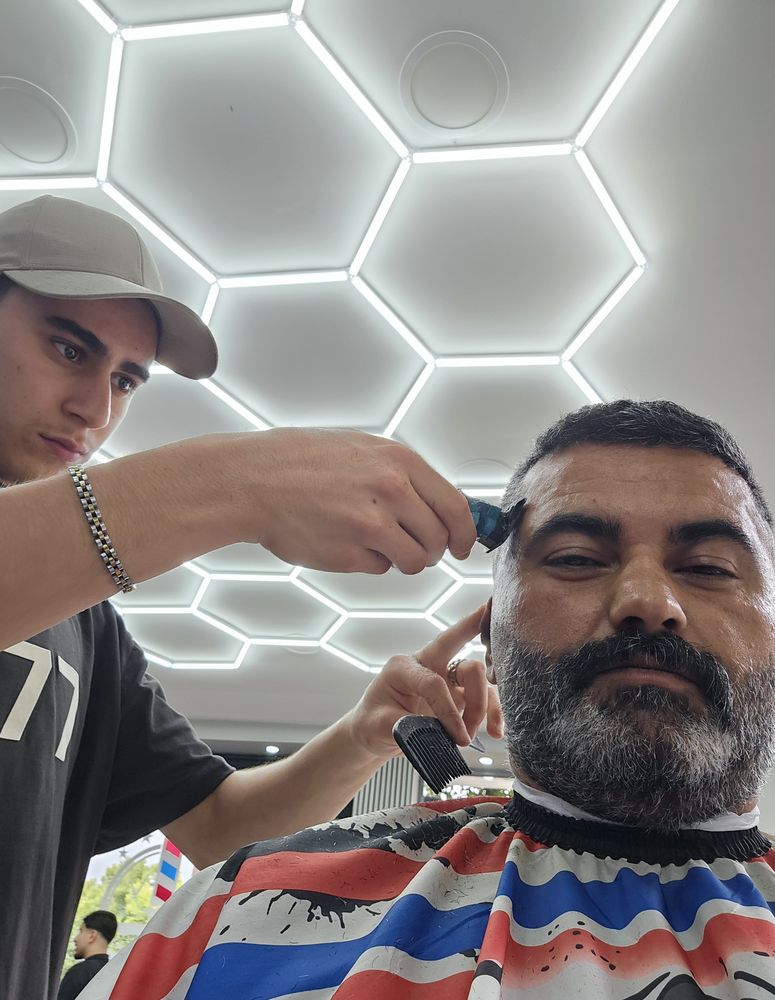 Barber detailing a client's beard with a trimmer under the salon's hex lighting